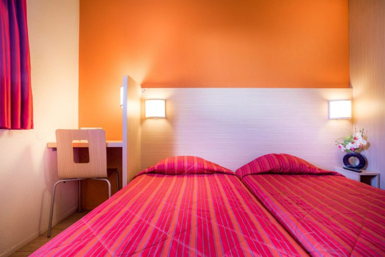 Chambre d'hôtel avec lits jumeaux et bureau.