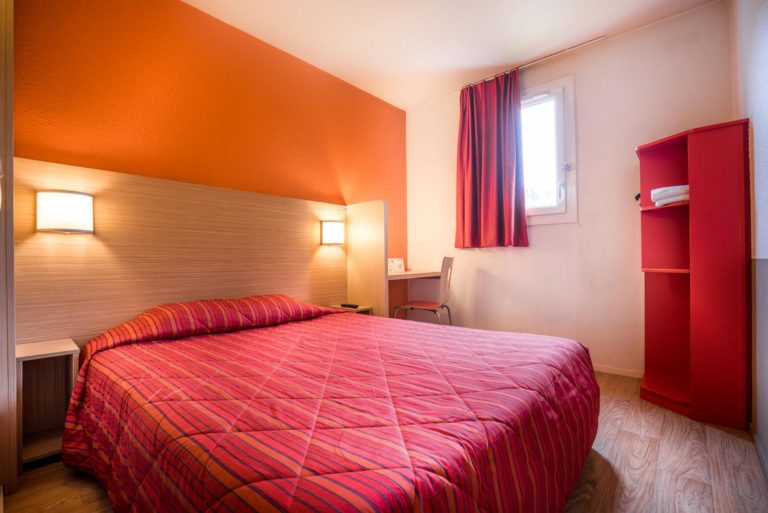 Chambre lit double avec décor rouge et orange.