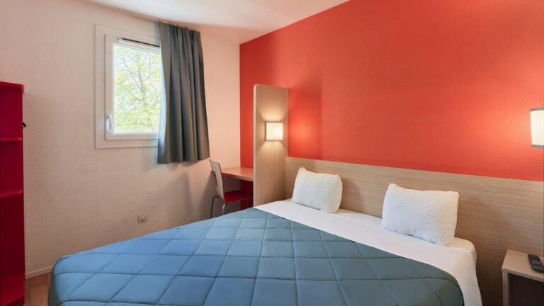 Chambre d'hôtel avec lit double et mur rouge.